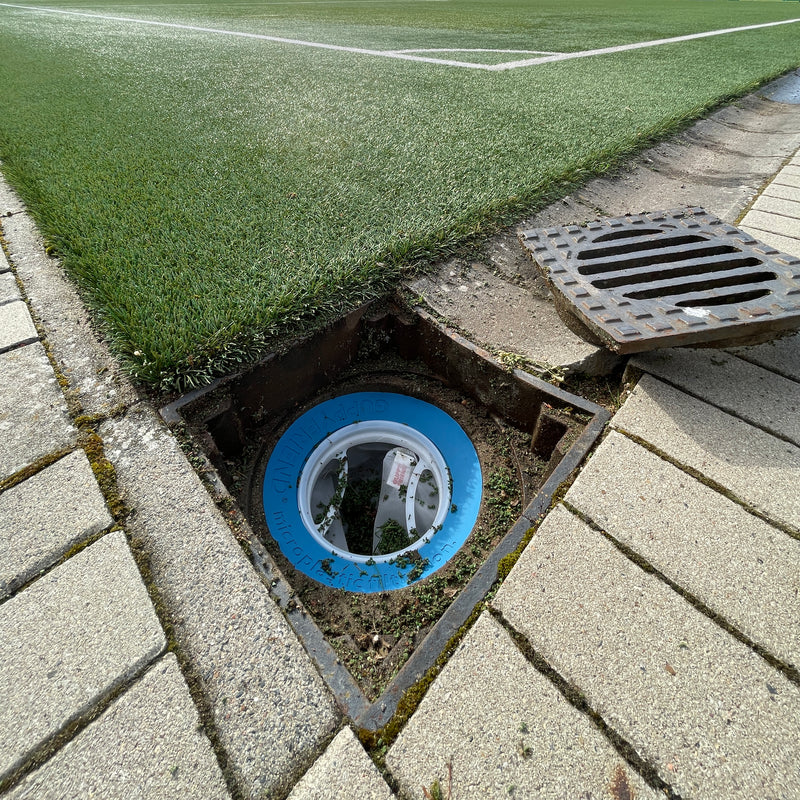 Wasserabfluss an einem Fußballplatz. In dem Abfluss befindet sich ein Guppyfrien Kunstrasen Filter, wo drin sich Infill Material angesammelt hat.