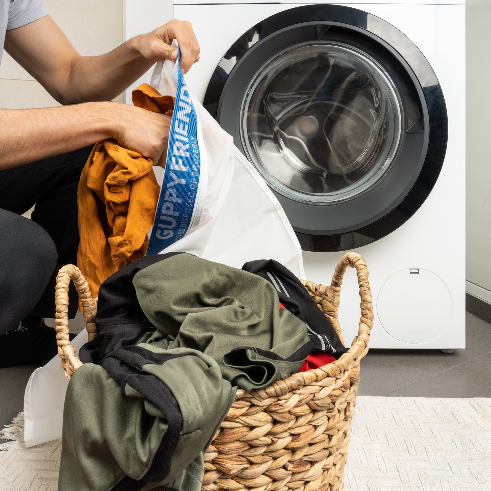 Eine Person packt  Wäsche in den Guppyfriend Waschbeutel vor einer Waschmaschine.