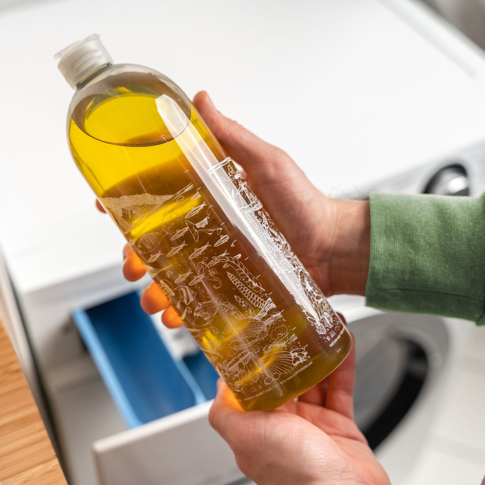 Person die Guppyfriend Waschmittel in der Hand hält vor einer Waschmaschine.